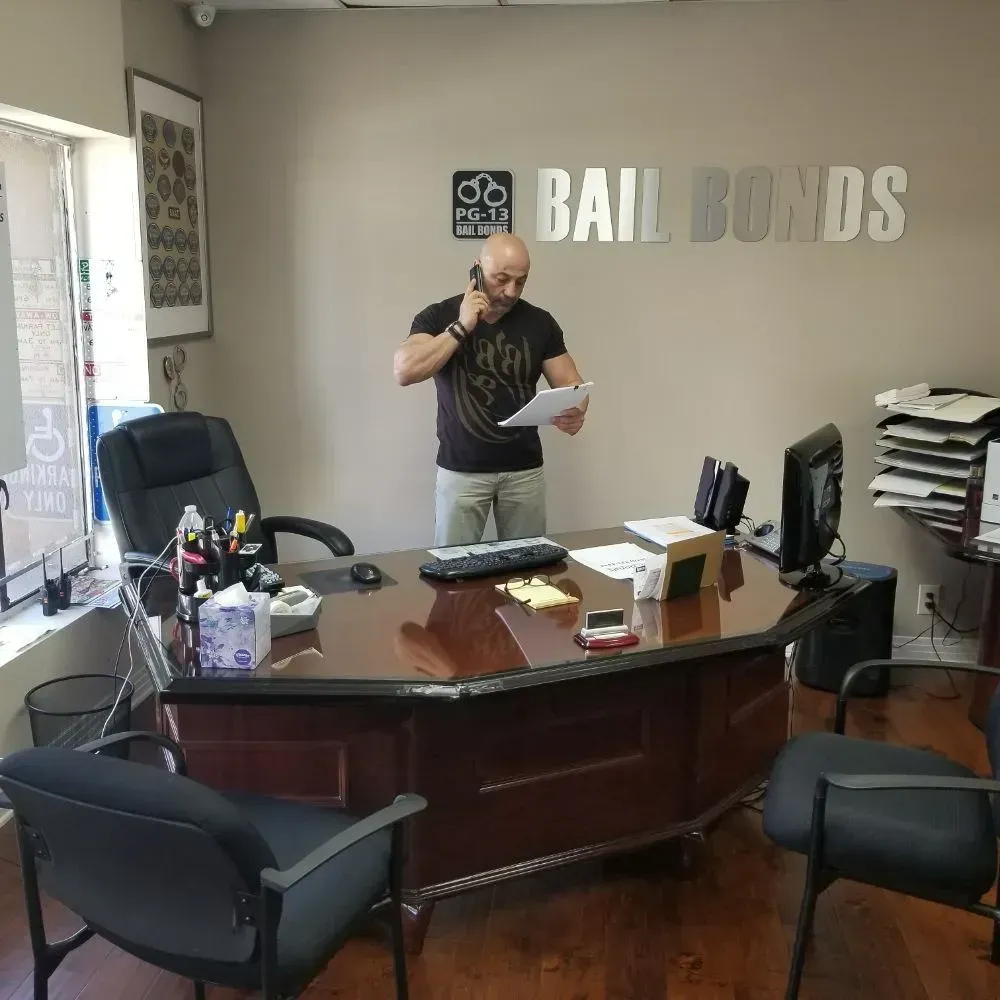 Man standing in an office behind a desk, reading a paper and speaking on the phone.