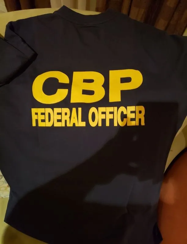 A cbp federal officer t-shirt is laying on a bed