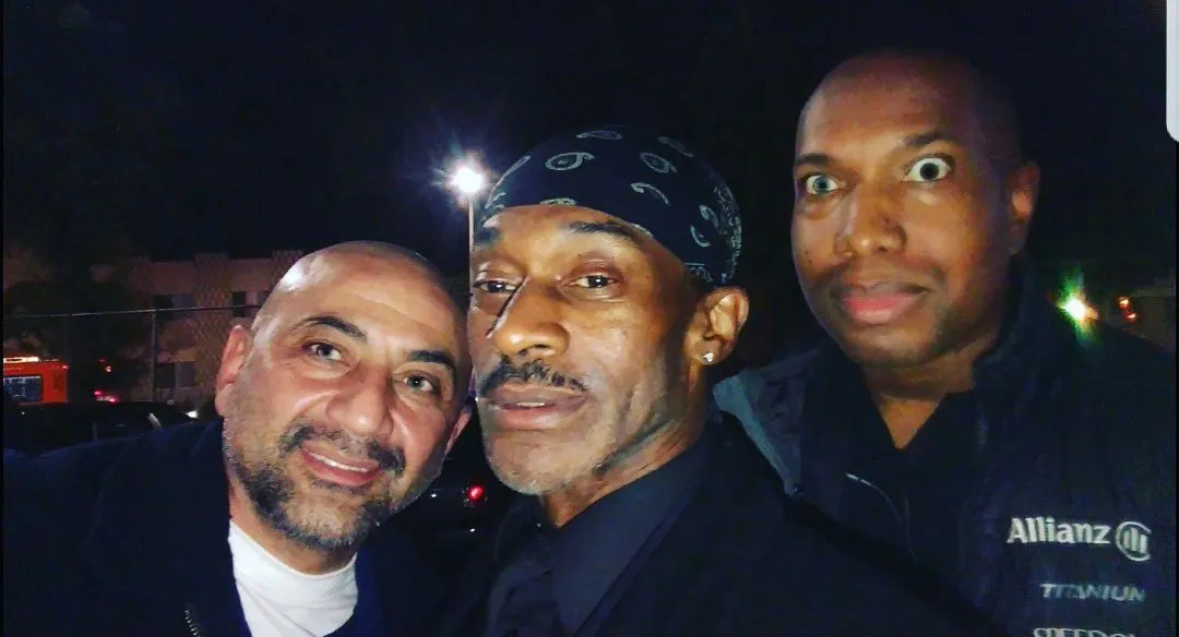 Three men posing for a picture with one wearing a bandana that says allianz