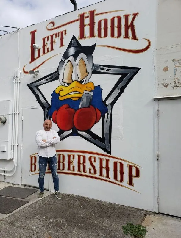 A man stands in front of a left hook barbershop mural